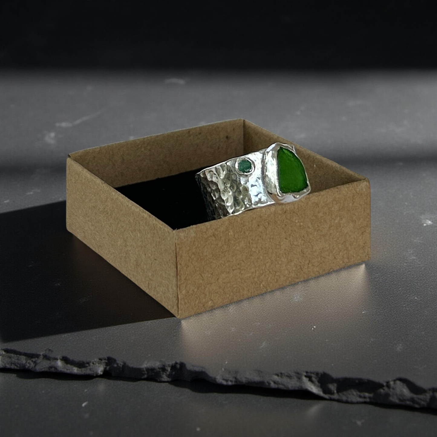 Silver ring with a green stone in a brown box on a dark surface