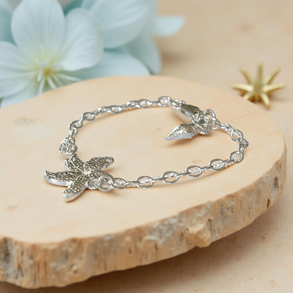 Silver bracelet with starfish design on a wooden surface with flowers in the background