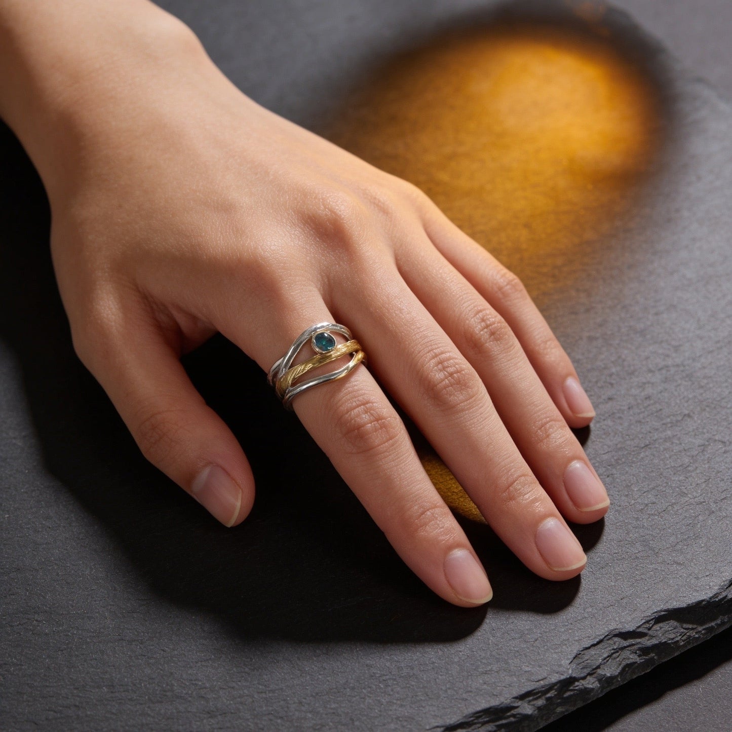 Hand wearing a ring with a blue stone on a dark surface