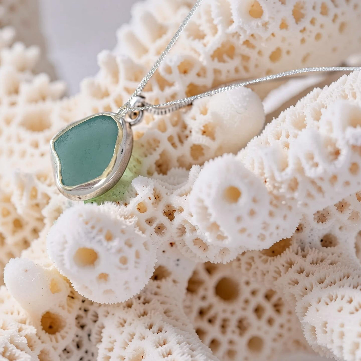 A silver-toned necklace with a smooth, rounded sea glass pendant in a soft mint green color, displayed on a textured white coral branch.